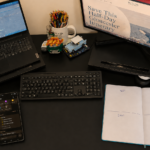 Warm home office desk with a phone displaying reminders, an open notebook labeled Keep, Edit, Drop and Add One, coffee, sneakers and weights.