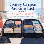Open suitcase packed for a family of four with cruise clothes, backpacks, passports, sun hat and travel essentials inside a bright ocean-view cruise cabin.
